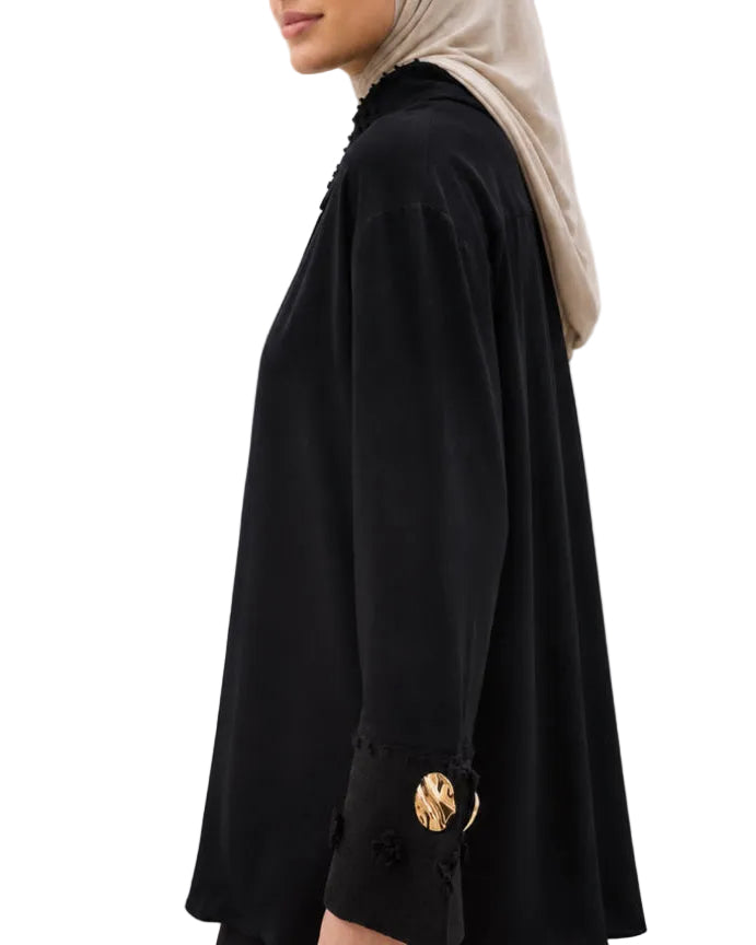 Gros plan sur le poignet texturé et le bouton doré chic de la chemise noire.