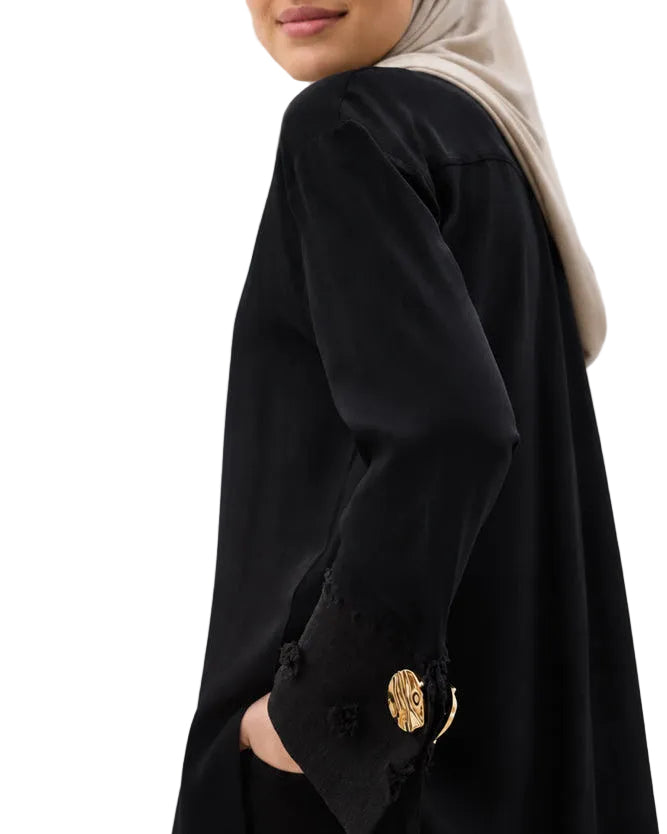 Gros plan sur le poignet texturé et le bouton doré chic de la chemise noire.